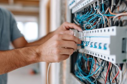 Electrician installing wiring in electrical panel. Professional technician connecting cables and circuits during residential construction and renovation work.